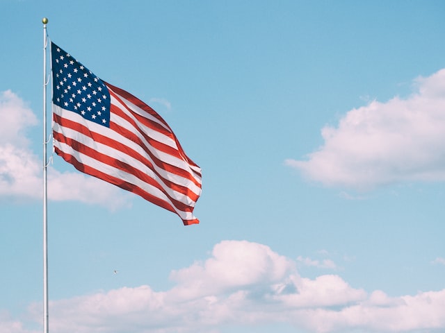 An American flag flying with clouds and a blue sky behind 
